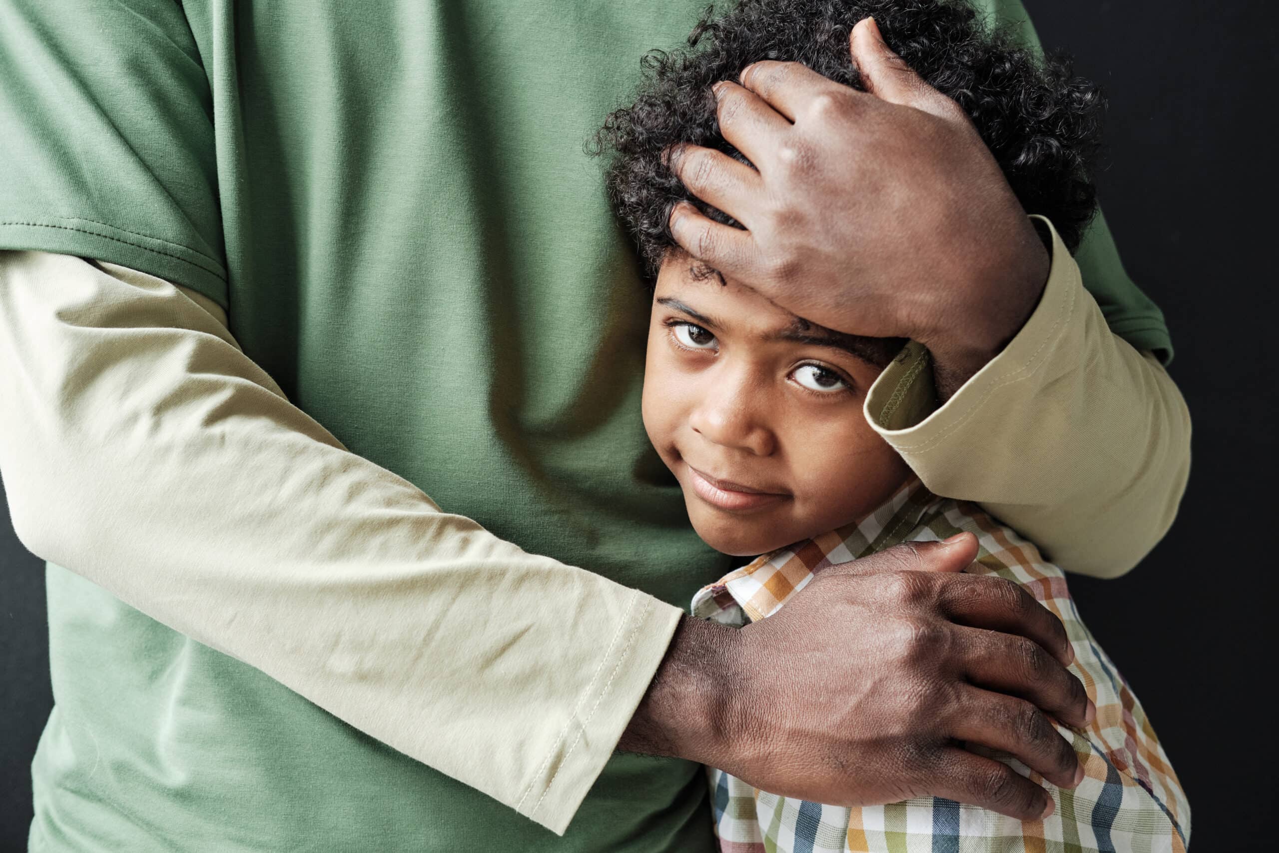 Close-up of a little boy being hugged by a parent.