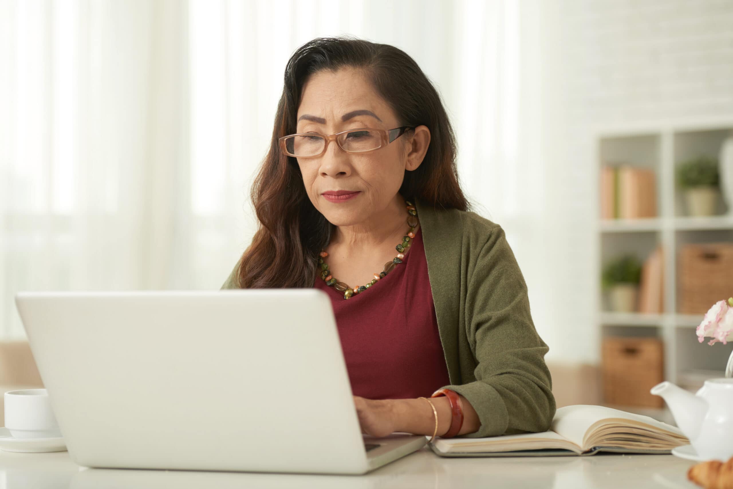 Mature woman wearing glasses using laptop at the table at home.