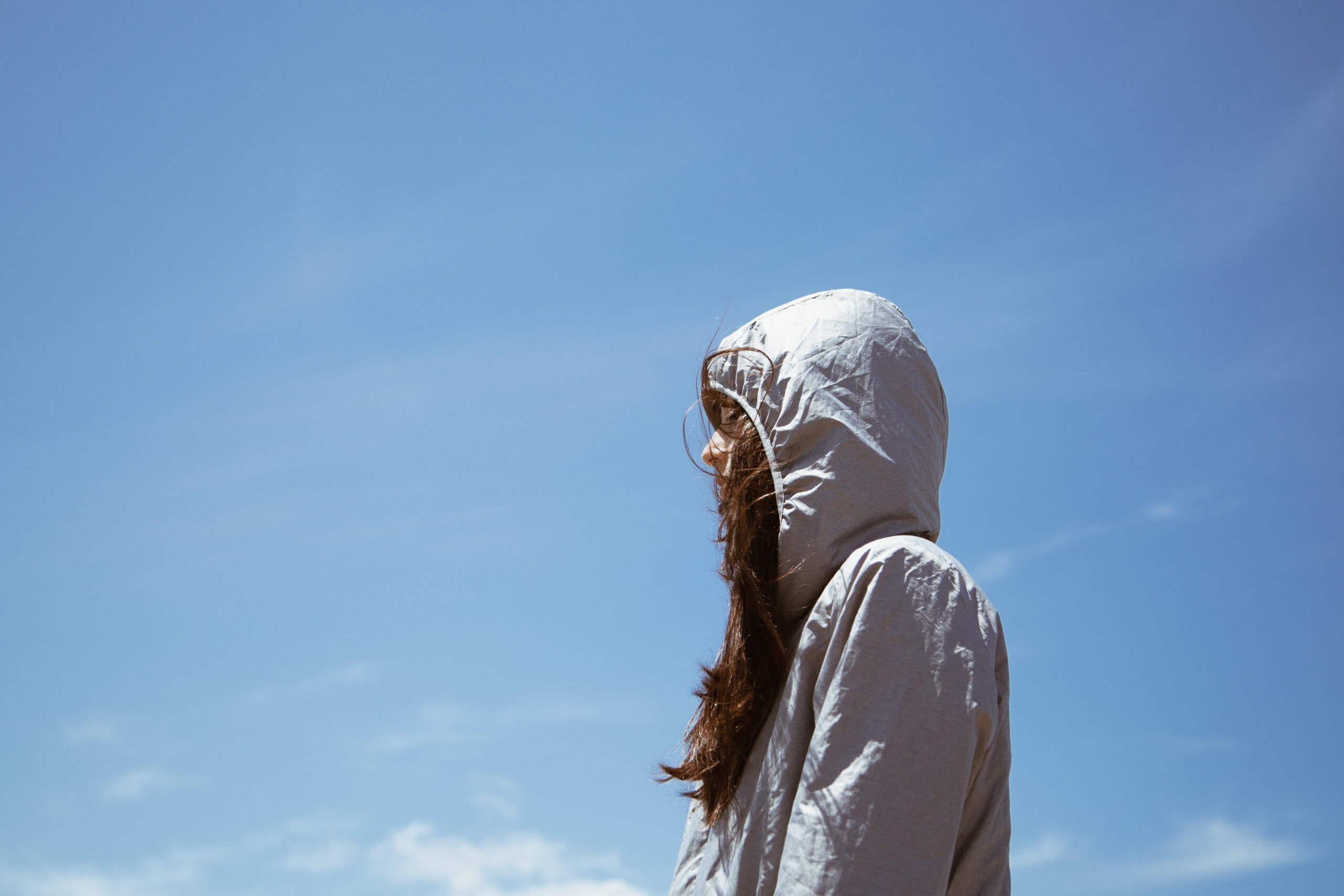 A young girl stands outside in a hoodie with the hood up.