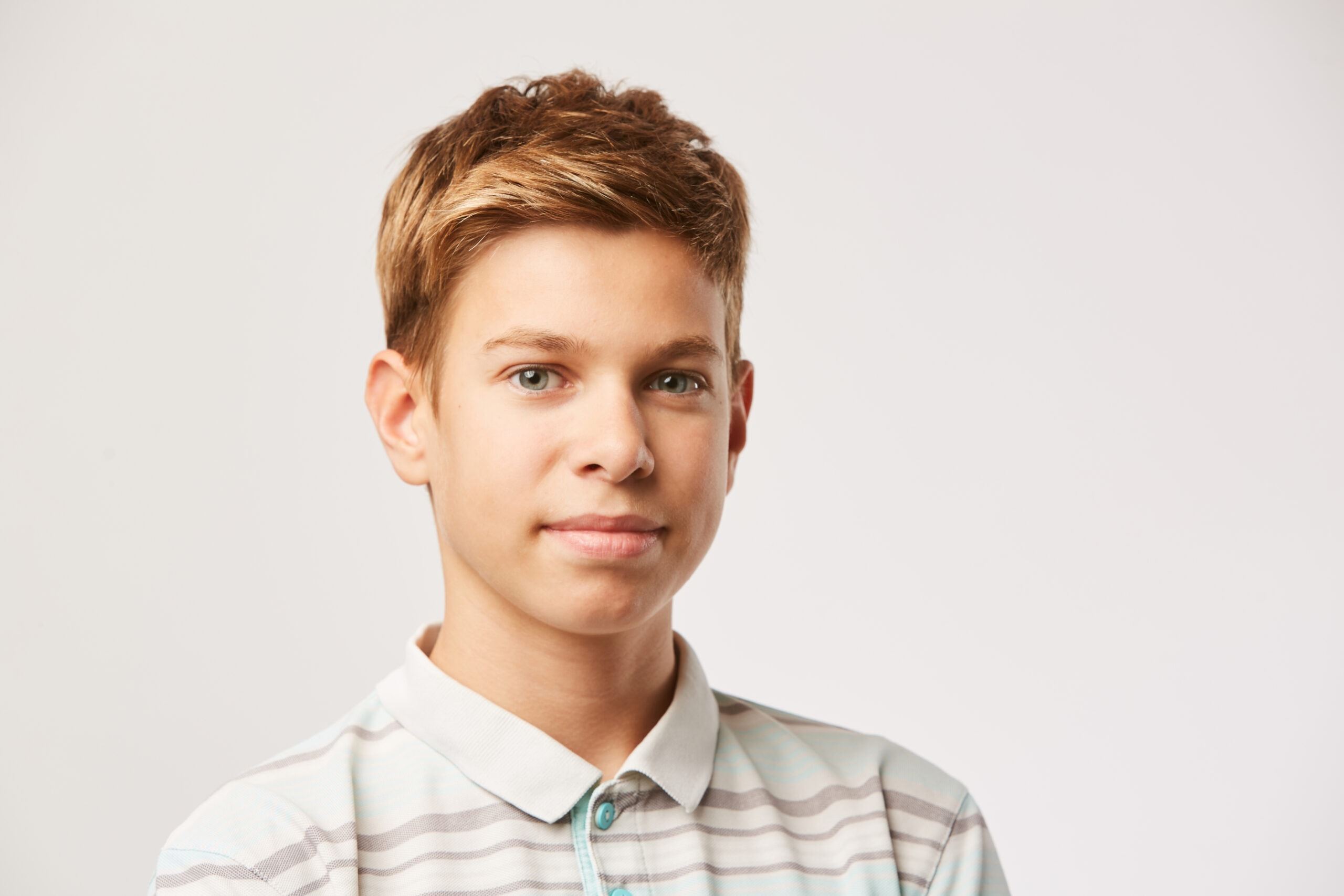 A portrait of a young boy, looking at the camera in front of a white background