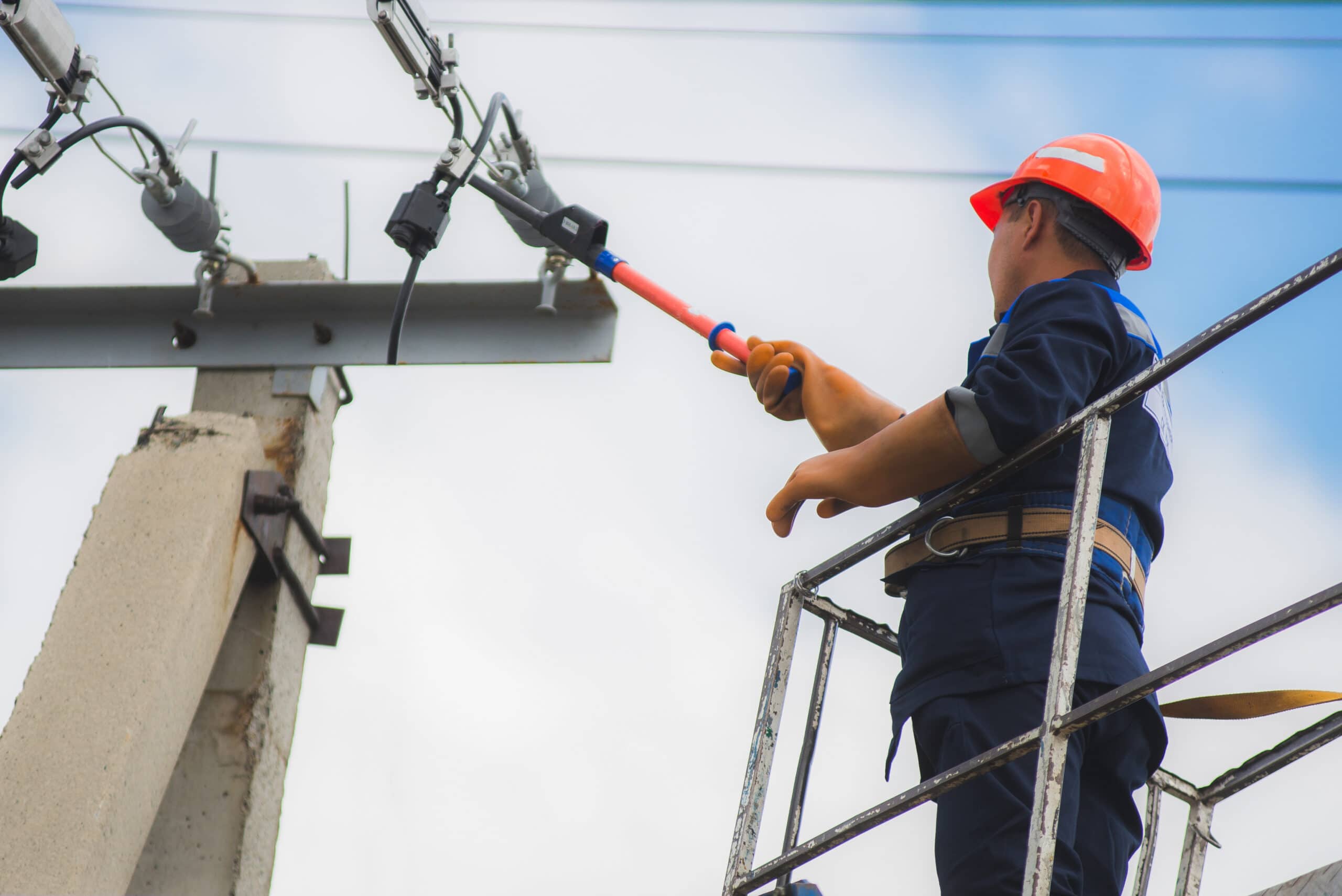 A person wearing a hard hat works on an electrical cable at height.