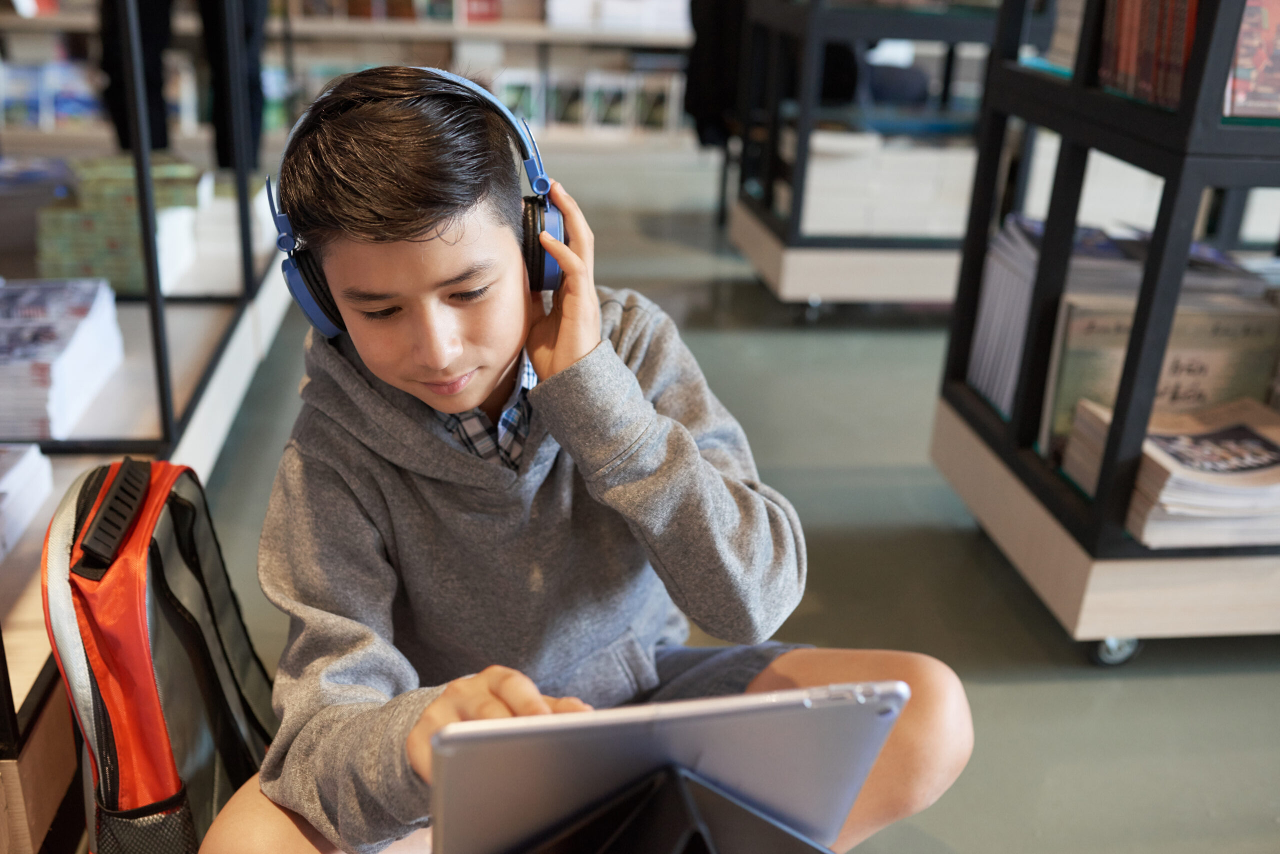 A teenage boy wearing headphones completes online work in the school library.