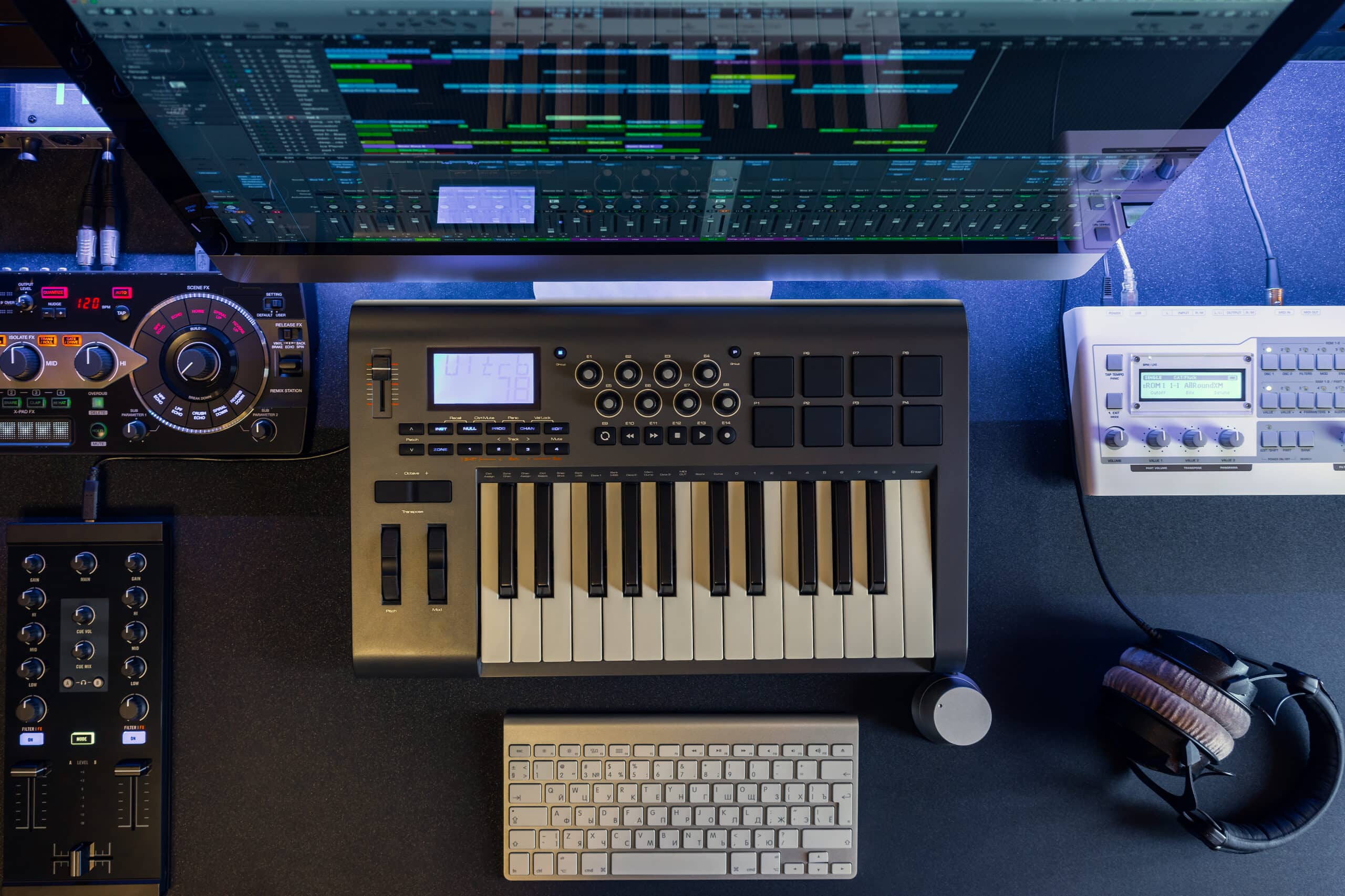 Overhead view of a music studio set up including keyboard, headphones and computer screen.
