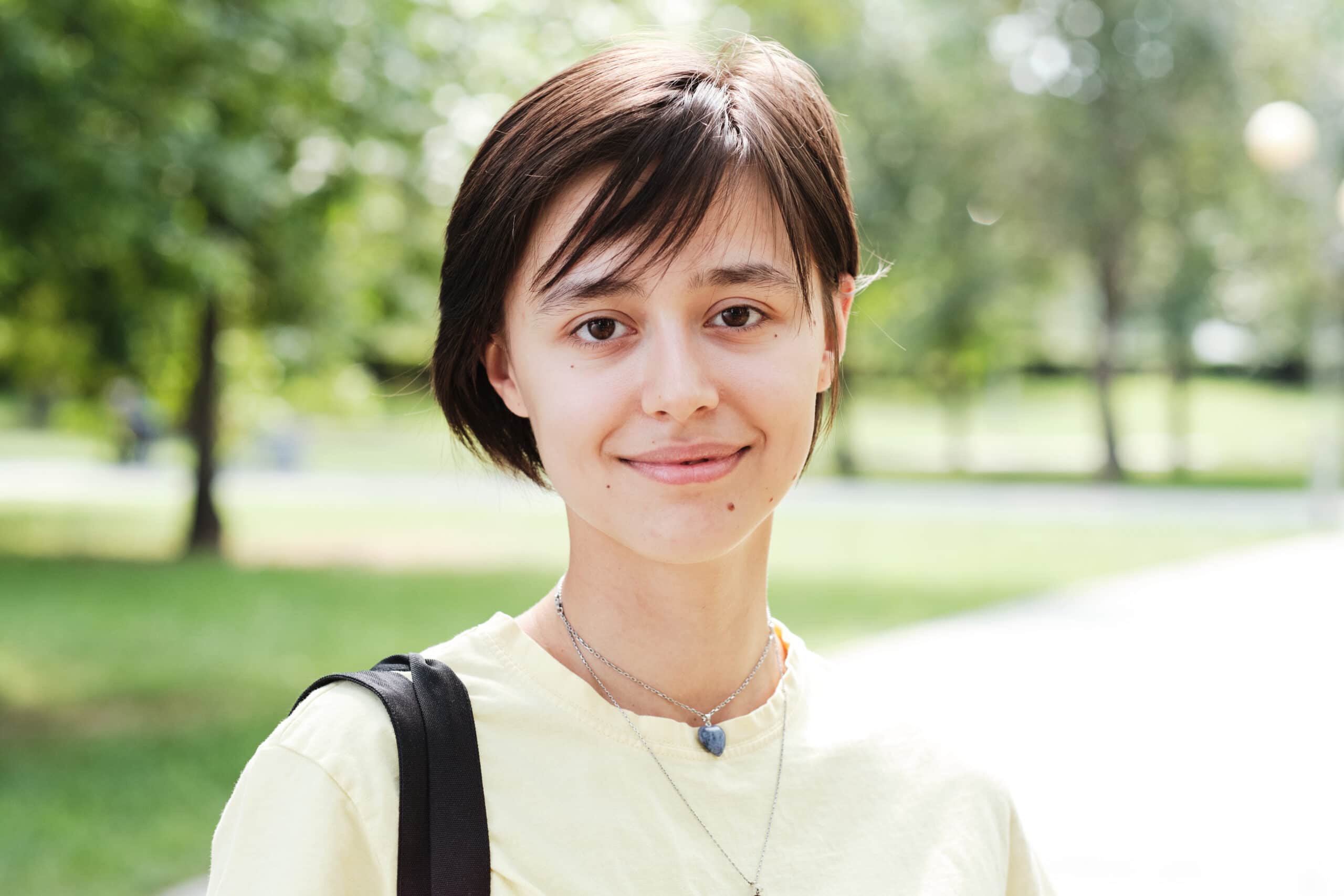 Close-up of a young woman with short hair looking at camera while standing outdoors on a sunny day.