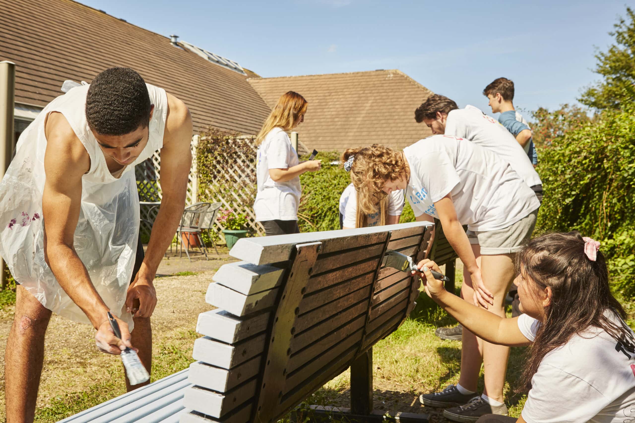 A group of young people work together to refurbish and paint a bench in their local community.