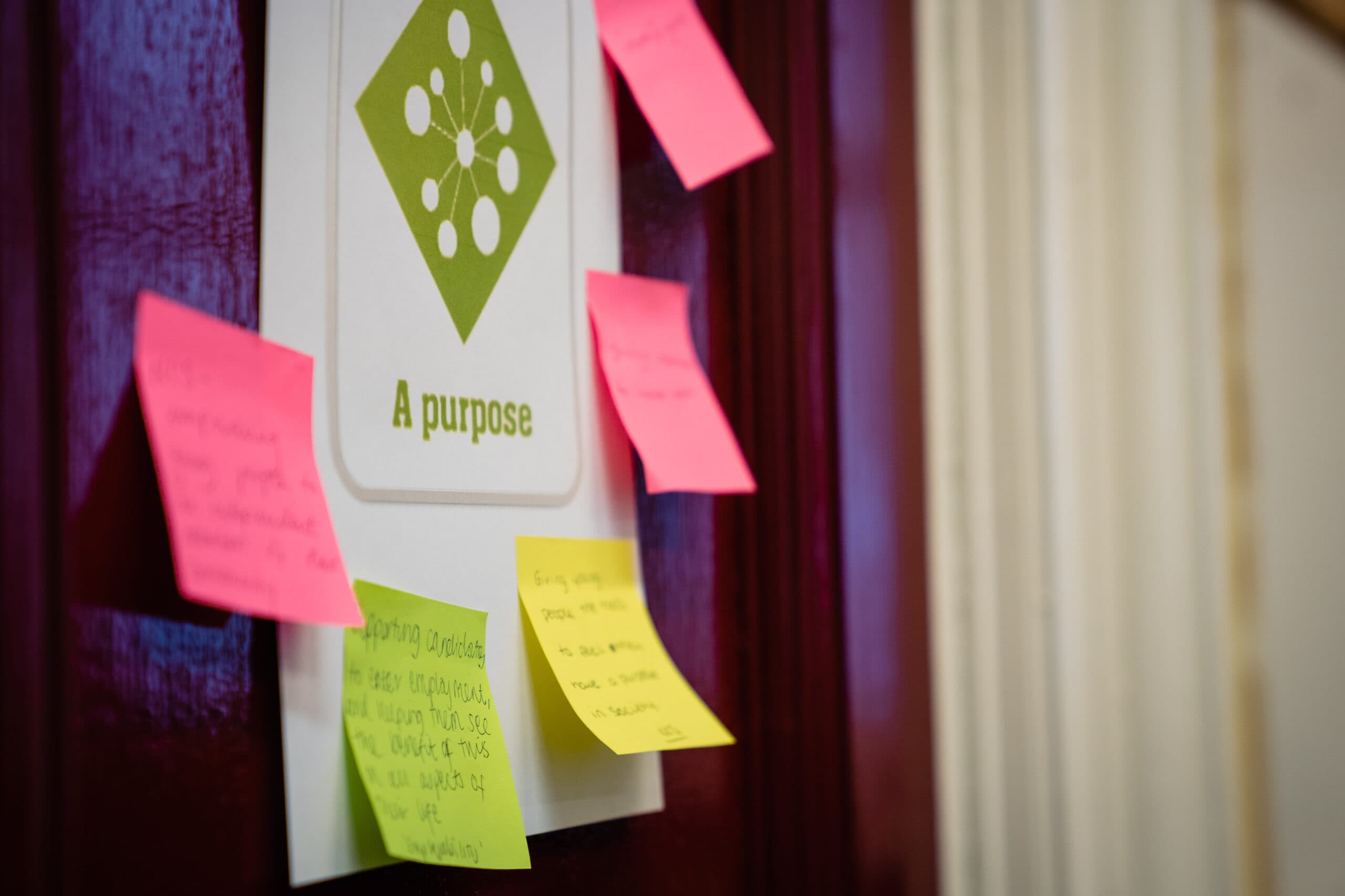 A poster stuck on the wall reads "A purpose". Around it are post-it notes where people have written what "purpose" means to them. None of the post-it notes are legible.