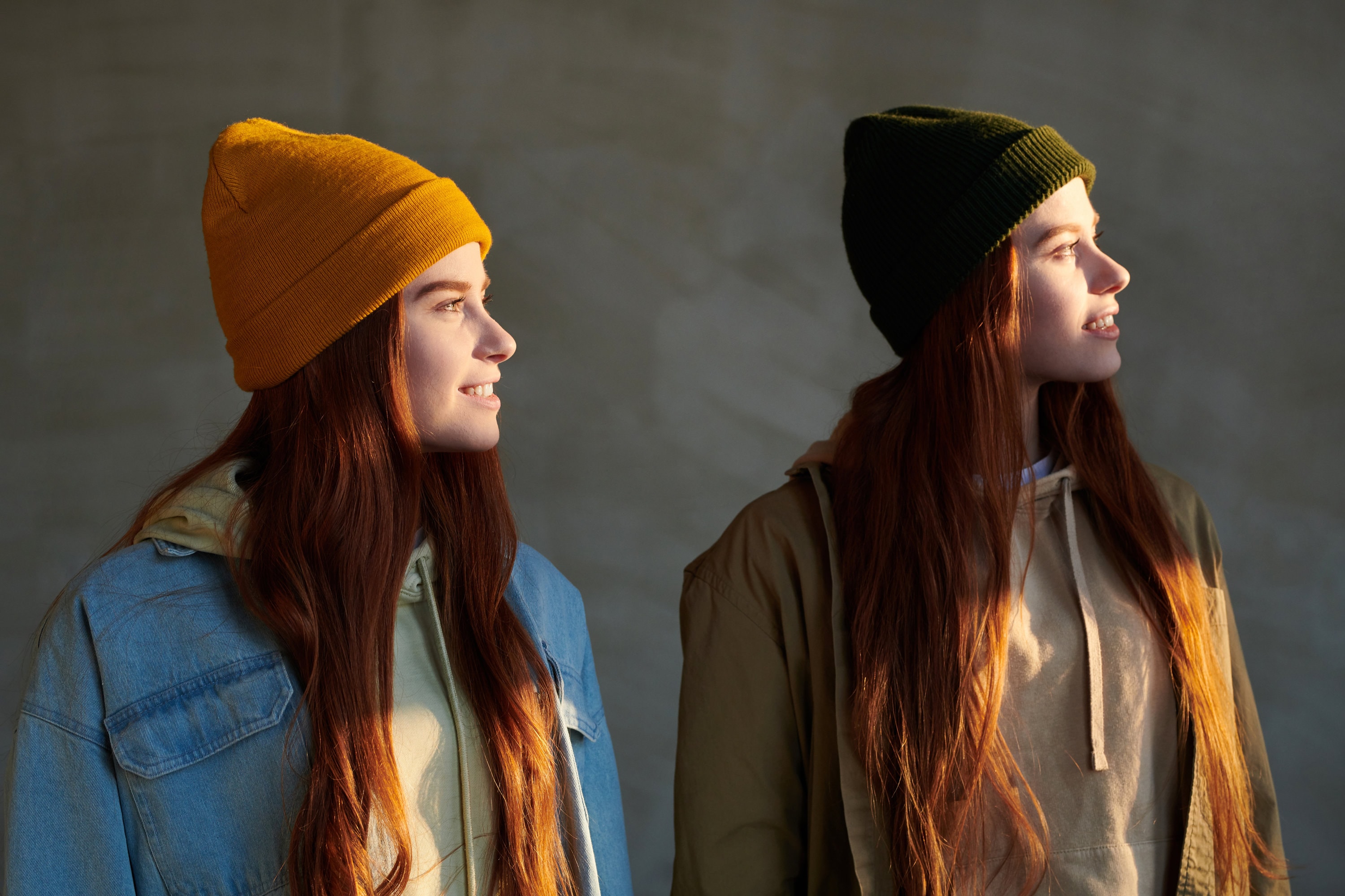 Female twins wearing beanie hats look out into the distance.