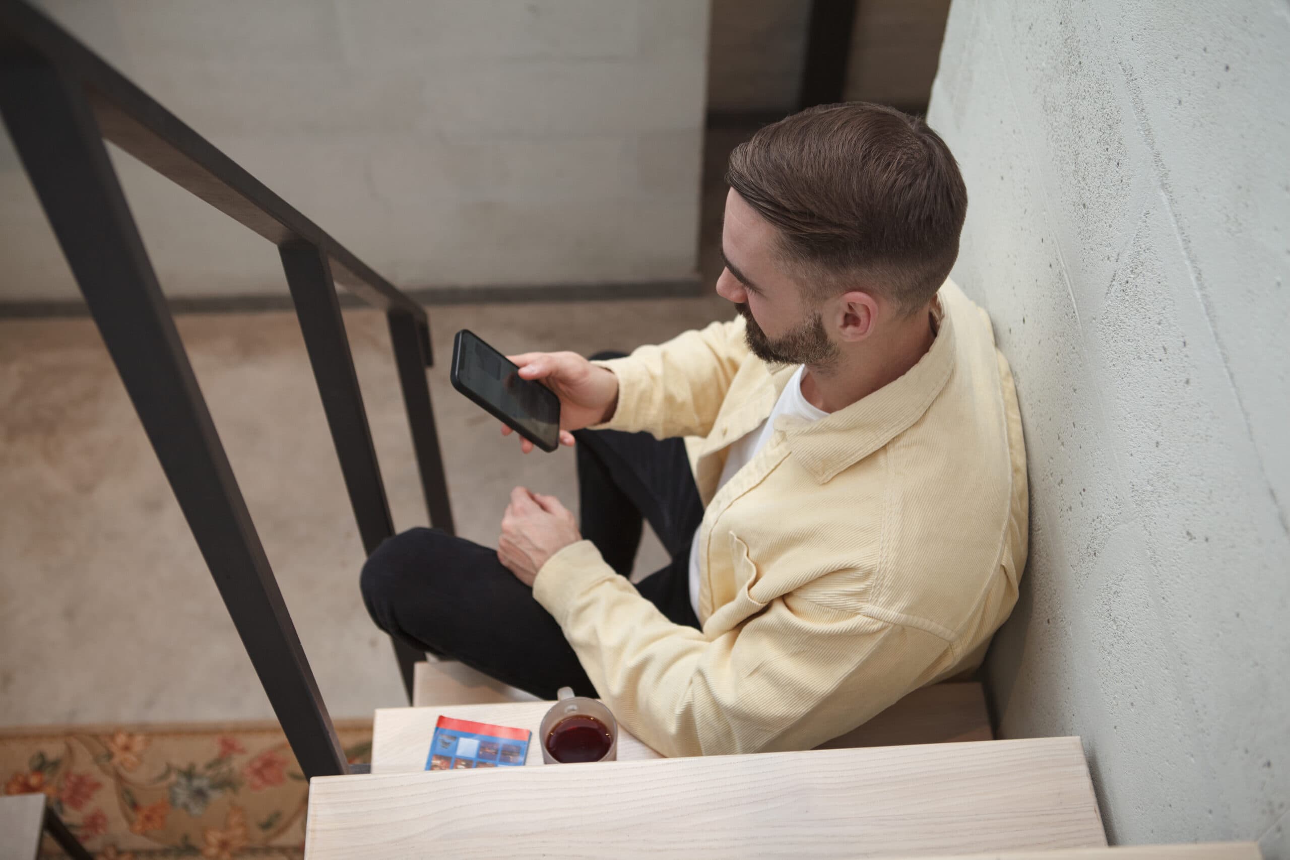Top view shot of a man texting on his smart phone, sitting on a staircase.