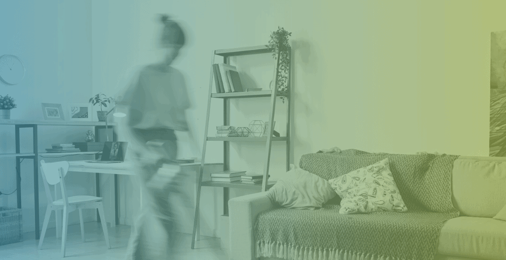 A woman walks through her living room. In the background, there is a desk and a sofa. The woman is blurred as she moves past the camera.