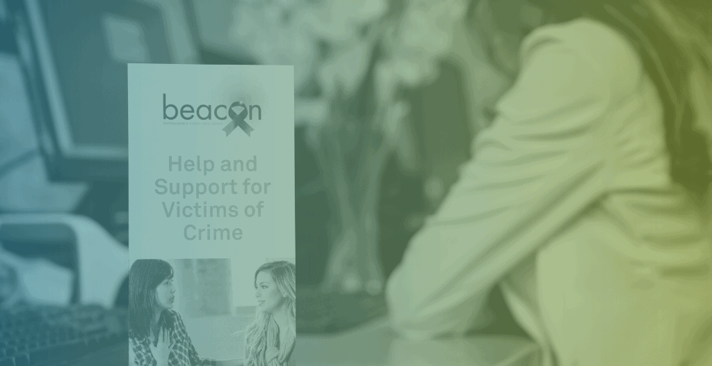 Close-up of a leaflet which reads "Help and support for victims of crime" while a member of staff works at a computer in the background.