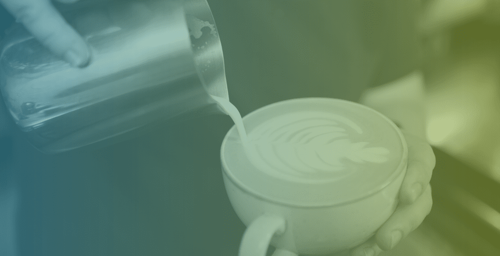 Close-up of a milk jug pouring milk into a small coffee cup.