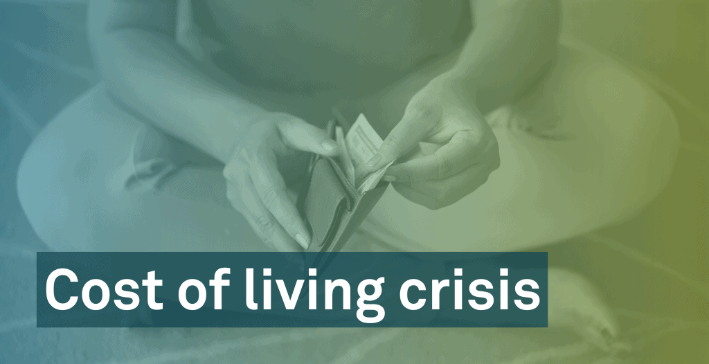 Close-up of hands opening a wallet. The words "Cost of Living Crisis" are overlaid on the top.