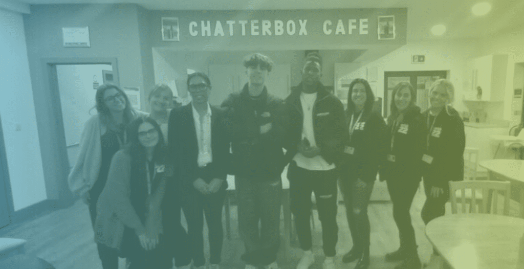Flintz and T4ylor pose beneath the Chatterbox Cafe sign, together with staff from Catch22's Derby and Derbyshire CARES team in Catch22 uniform.