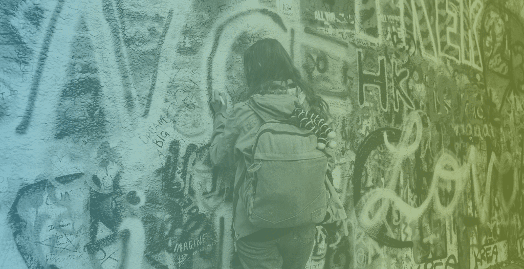 A young woman, wearing a backpack, adds to a wall covered in graffiti.