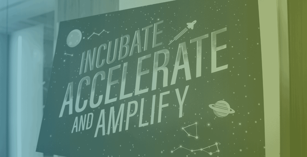 A sign is positioned on an easel which reads "Incubate, Accelerate and Amplify". The sign looks like the night sky, with star constellations, planets and a rocket depicted around the edges.