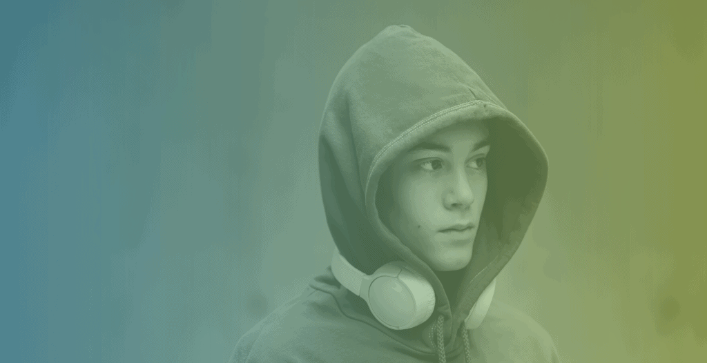 A portrait of a young man wearing a blue hoodie with the hood up, and wireless headphones round his neck.