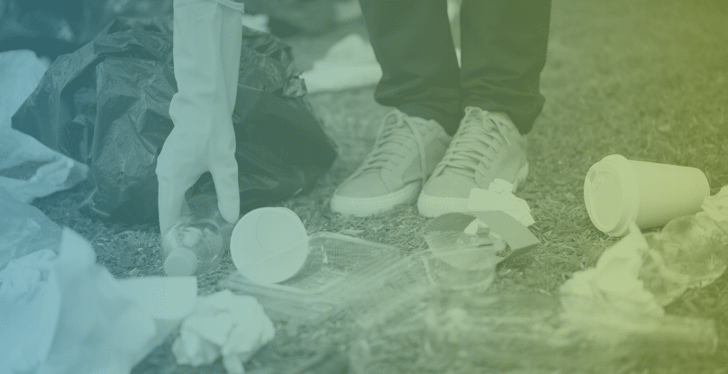 Close-up of a person bending down to pick up litter in the park. Their feet and a gloved hand can be seen.