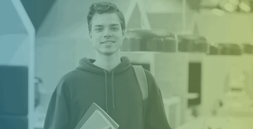 A young male student smiles directly at the camera. He has a backpack over one shoulder and books in the other hand.