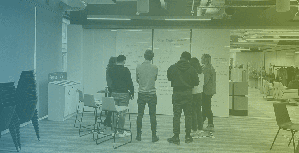 A group of entrepreneurs gather around a full-height white board, collaborating on potential solutions to issues that have been raised.