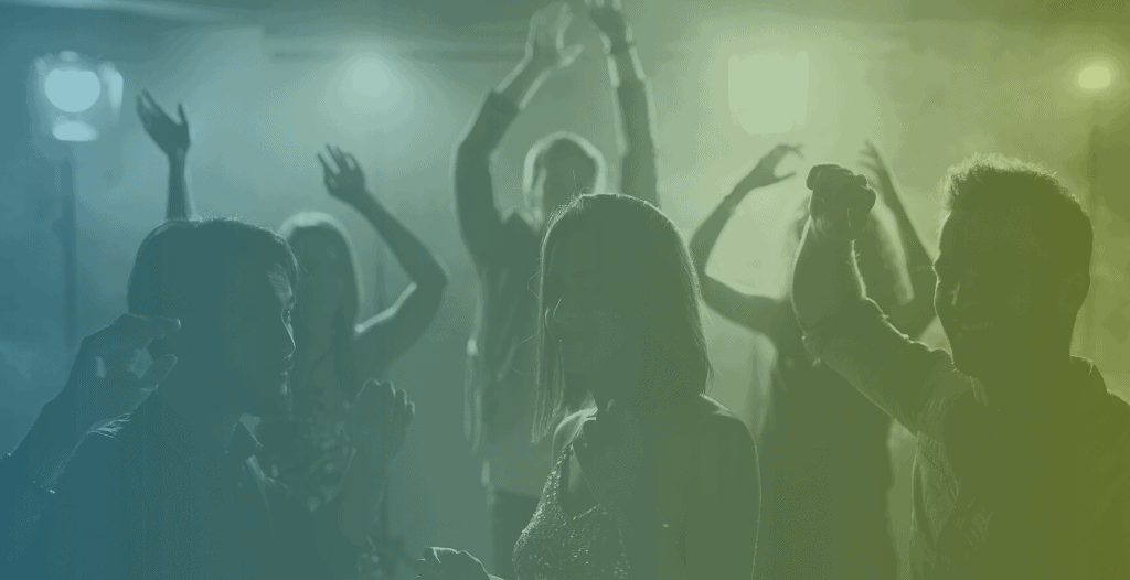Young people dance in a darkened room. None of their features are visible due to the lighting.