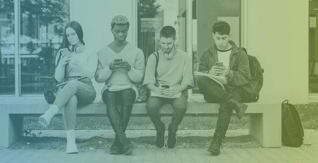 Four students sit on a bench. They are not talking to each other or making eye contact, paying attention instead to their phones.