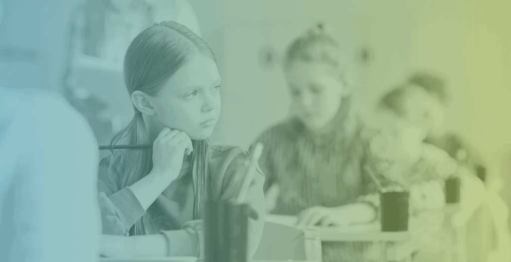 A young girl, sitting at a school desk, looks thoughtfully out of the window, holding a pencil in their hand as they rest their head on their hand. Other students can be seen in the background.