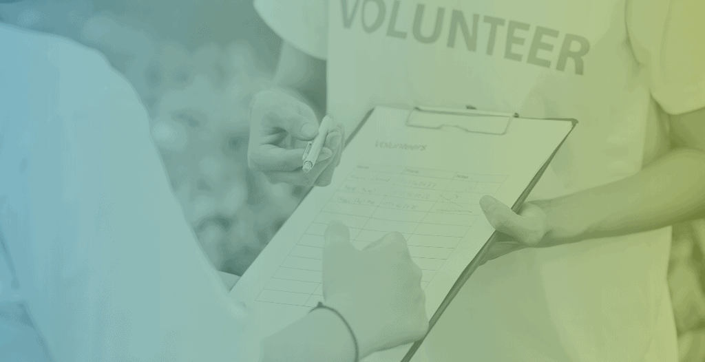A person wearing a "Volunteer" t-shirt holds out a clipboard to someone who is signing up to offer their time.